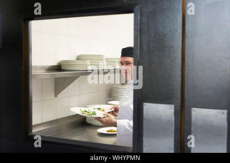 Ritratto di un sorridente chef maschio il contenimento di cibo piastre in cucina Foto Stock