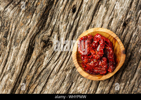 Terrina di pomodori seccati al sole su sfondo di legno, vista dall'alto piatto o laici. Composizione minima Foto Stock