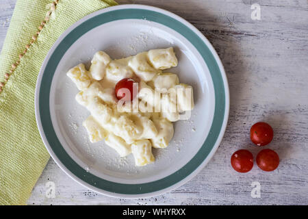 Piastra bianca di crema calda gnocchi di patate servita con pomodorini/ posate/ cibo sullo sfondo - Immagine Foto Stock