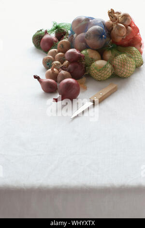 Un assortimento di cipolle in rete sulla tabella Foto Stock