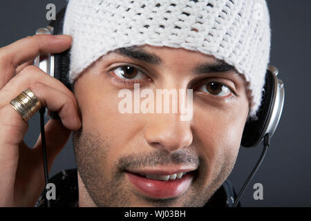 Closeup ritratto del bel giovane uomo che indossa knit hat e cuffie su sfondo grigio Foto Stock