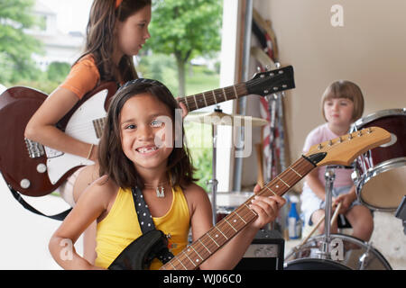 Ritratto di Allegro giovane ragazza a suonare la chitarra con la band in garage Foto Stock