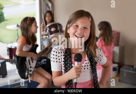 Ritratto di giovane carina ragazza cantare nel microfono con gli amici suonare uno strumento musicale in garage Foto Stock