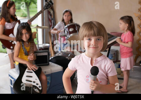 Ritratto di giovane carina ragazza con un microfono con gli amici suonare uno strumento musicale in garage Foto Stock