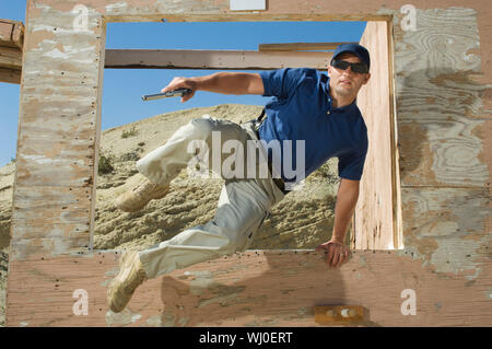 Uomo con pistola a mano jumping ostacolo al poligono di tiro Foto Stock