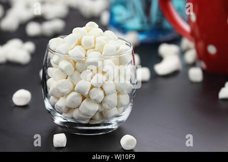 Bicchiere di mini marshmallows con tazza di cacao in background. Estrema profondità di campo. Foto Stock