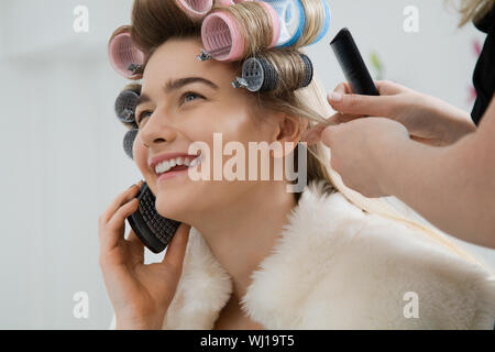 Felice modello femminile usando il cellulare mentre avente i suoi capelli arricciati Foto Stock
