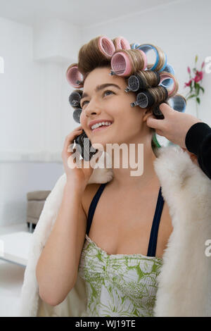 Felice modello femminile usando il cellulare mentre avente i suoi capelli arricciati Foto Stock