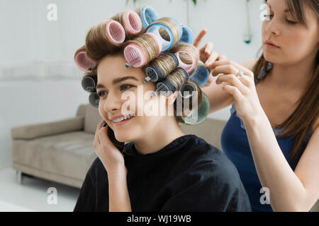 Felice modello femminile usando il cellulare mentre avente i suoi capelli arricciati Foto Stock