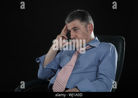 Angry businessman in camicia e cravatta seduto su sfondo nero Foto Stock