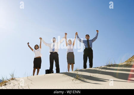 Basso angolo di vista business multietnica di persone in piedi insieme alzando le mani nel deserto Foto Stock