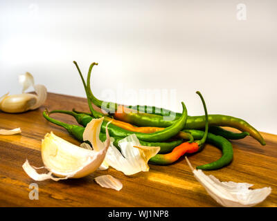 Peperoncino e aglio e aglio pelle sul piatto di legno e sfondo luminoso. Messa a fuoco selettiva. Foto Stock