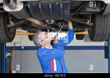 Meccanica auto lavora al di sotto di una macchina utilizzando una chiave inglese Foto Stock