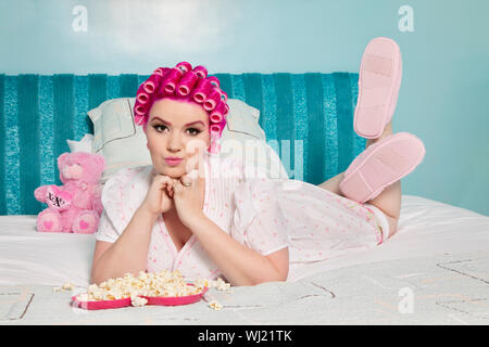 Ritratto di giovane donna sdraiata sul letto con il popcorn Foto Stock