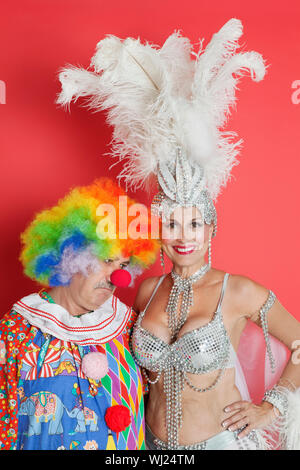 Ritratto di felice senior showgirl con triste clown in piedi contro lo sfondo rosso Foto Stock