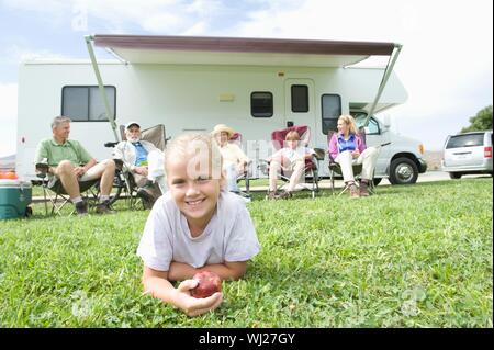 Ritratto di una incantevole piccola ragazza distesa sull'erba con la famiglia al di fuori seduta RV home Foto Stock