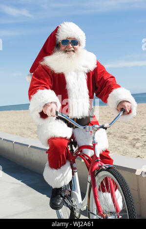 Ritratto di un felice senior Babbo Natale ciclo di equitazione da spiaggia Foto Stock