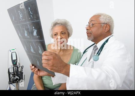 Un americano africano medico maschio spiegando x-ray relazione al paziente presso la clinica Foto Stock