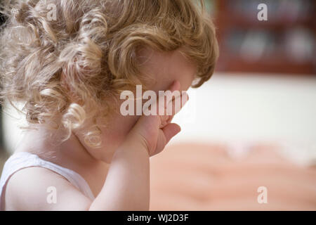 Primo piano vista laterale della infelice baby boy occhio di sfregamento a casa Foto Stock