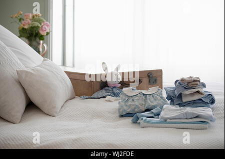 I bambini vestiti di ripiegato sul letto accanto alla valigia in camera da letto Foto Stock