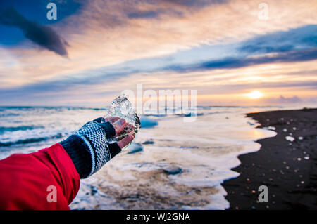 Traveler holding pezzo di ghiaccio sulla spiaggia di diamante in Islanda durante il tramonto Foto Stock