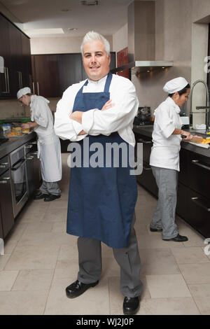 A piena lunghezza Ritratto di certi chef maschio con i colleghi che lavorano in cucina commerciale Foto Stock