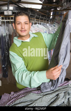 Ritratto di giovane proprietario di lavanderia esaminando magliette al contatore Foto Stock