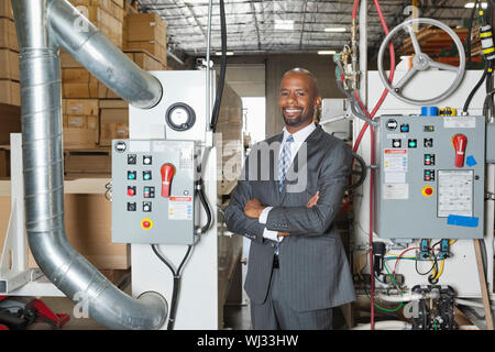 Ritratto di African American businessman in piedi con le braccia incrociate con i macchinari in background Foto Stock