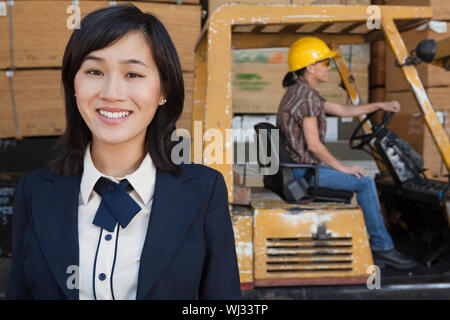 Ritratto di donna sorridente mentre femmina lavoratore industriale la guida carrello elevatore a forche in background Foto Stock