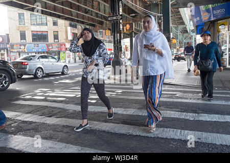 Due abiti elegantemente le donne in hijabs attraversare una strada a Roosevelt Ave. sotto la metropolitana sopraelevata. Jackson Heights, Queens, a New York City. Foto Stock