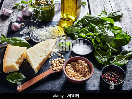 Di foglie di basilico fresco, parmigiano grattugiato, pinoli, aglio, pepe, bottiglia di olio di oliva su una tavola in legno rustico con fatti in casa pesto di basilico sau Foto Stock