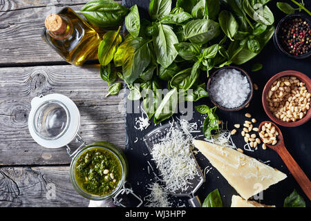 Di foglie di basilico fresco, parmigiano grattugiato, pinoli, aglio, pepe, bottiglia di olio di oliva su una tavola in legno rustico con fatti in casa pesto di basilico sau Foto Stock