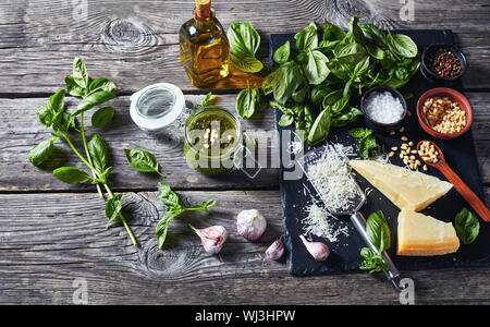 Classico pesto di basilico salsa in un vasetto di vetro. di foglie di basilico fresco, parmigiano grattugiato, pinoli, aglio, pepe in una ciotola su di un legno rustico tabl Foto Stock