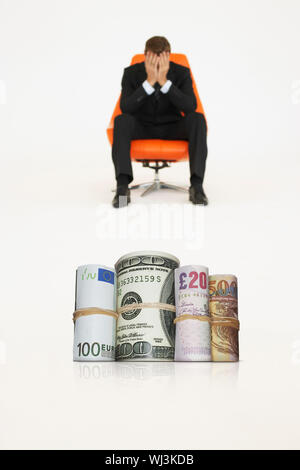 Rotoli di denaro con imprenditore preoccupato su una sedia che rappresentano problemi finanziari Foto Stock