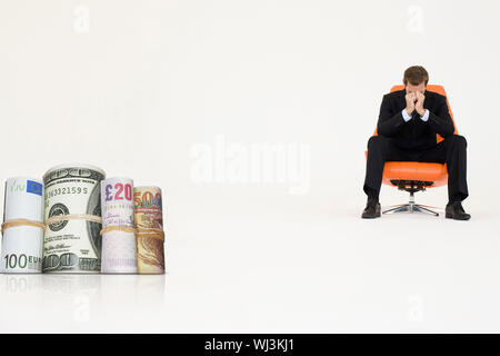 Rotoli di denaro con imprenditore preoccupato su una sedia che rappresentano problemi finanziari Foto Stock