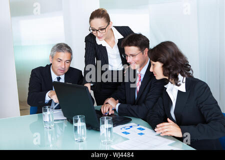 Business team professionale di uomini e donne hanno una riunione si sono riuniti intorno a un computer portatile circondato da letteratura Foto Stock