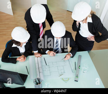 Vista aerea di un gruppo di architetti e ingegneri strutturali a discutere un piano disposto sul tavolo di fronte a loro Foto Stock