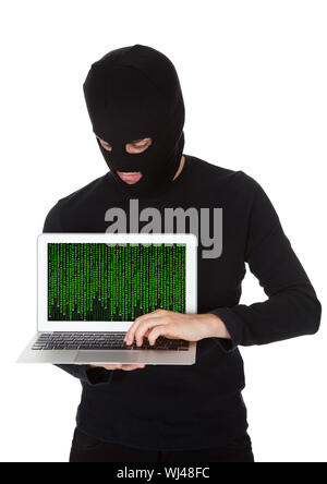 Hacker vestita di nero con una maschera in piedi al furto di dati da un computer portatile con lo schermo rivolto verso la fotocamera in una violazione della sicurezza Foto Stock