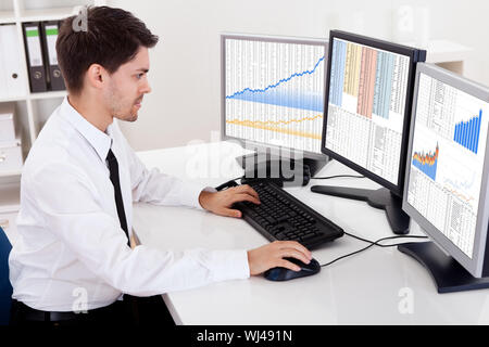 Al di sopra della spalla vista degli schermi di computer di uno stock broker trading in un mercato rialzista che mostra grafici ascendente Foto Stock