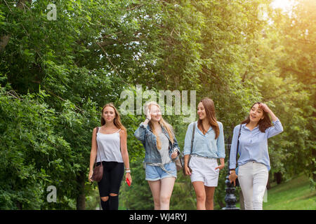 Quattro eleganti amici giovani donne a parlare e a camminare insieme sulla passerella con alberi Foto Stock