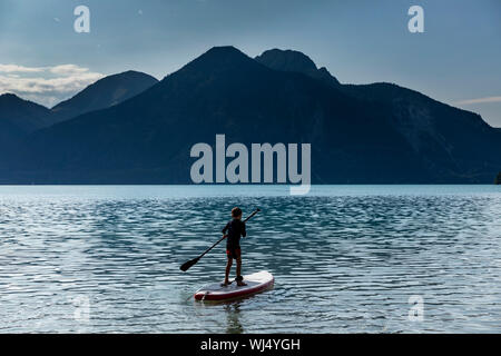 Ragazzo paddleboarding sul soleggiato, idilliaco lago di montagna, Walchensee, Baviera, Germania Foto Stock