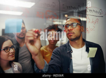 Un gruppo di imprenditori a discutere di lavoro e utilizzando la scheda di vetro per scrivere i piani aziendali in ufficio Foto Stock