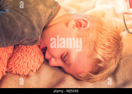 Un simpatico 5-anno-vecchio ragazzo stanchi dopo la partita e si è addormentato nel pomeriggio sul lettino con un orsacchiotto di peluche. Ritratto di un bambino al tramonto Foto Stock