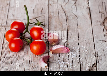 Pomodori ciliegini, aglio, pepe e sale in stile rustico sfondo di legno Foto Stock