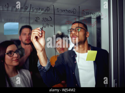 Business man iscritto sulla parete di vetro trasparente con i colleghi in attesa in ufficio Foto Stock