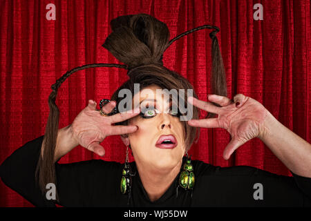 Eccentrico drag queen guardando verso l'alto con le dita vicino al viso Foto Stock