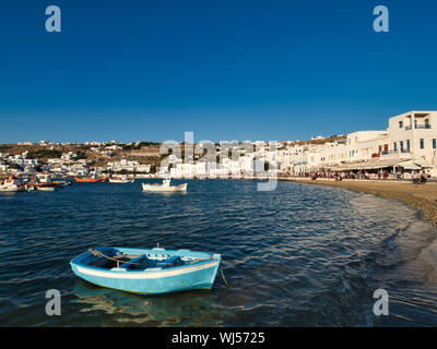 Varie navi galleggianti su increspa l'acqua di mare vicino alla costa e case bianche della città contro il cielo blu senza nuvole sull'isola di Mykonos in Grecia Foto Stock