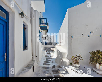 Stretto sentiero di pietra gong in prossimità degli edifici con pareti bianche sulla strada di piccola città contro il cielo blu senza nuvole sull'isola di Mykonos in Grecia Foto Stock