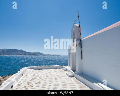 Ingresso della Chiesa di Agios Haralambos e pezzo di antica pietra terrapieno contro la calma il mare blu e il cielo senza nuvole sull'isola di Mykonos in Grecia Foto Stock