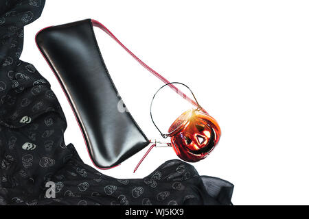 Festa di Halloween vestito femminile layout di accessori nero su sfondo bianco: borsetta, panno con teschi e vetro di zucca. Foto Stock
